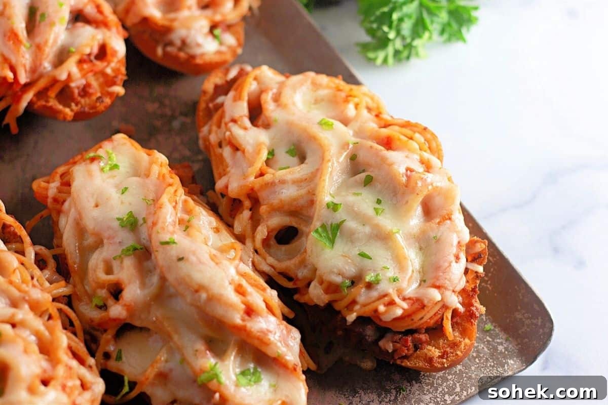 21 Quick Ground Beef Dinners That Will Have Everyone Asking Your Secret 10 Toasted bread slices topped with spaghetti, meat sauce, melted cheese, and garnished with chopped parsley on a metal baking sheet.