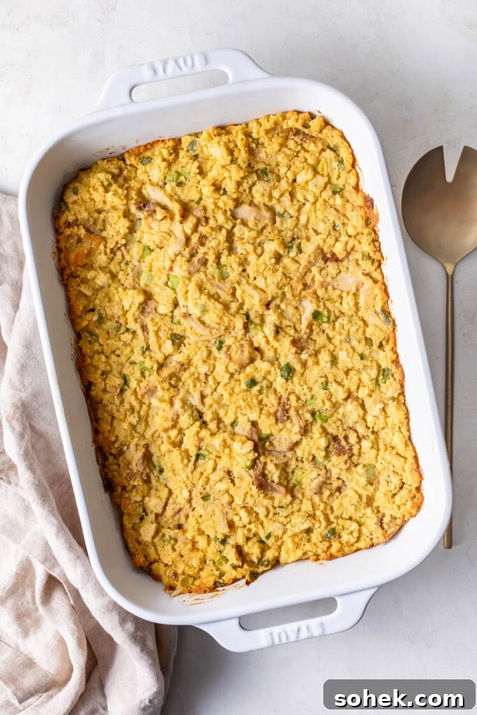 Chicken and cornbread dressing in a white casserole dish with a gold spoon and white dinner napkin