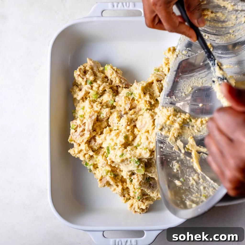 scooping the chicken and cornbread dressing mix into a white casserole dish. 