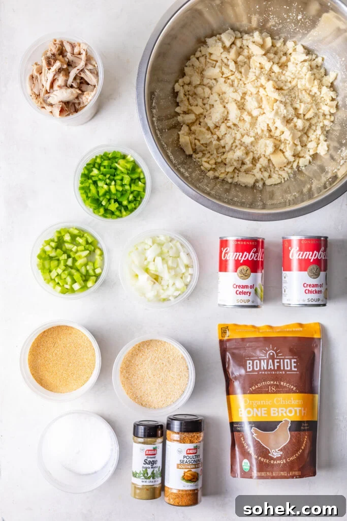 Cup of pulled chicken, broken up cornbread in a silver mixing bowl, bowl of diced celery, bowl of diced bell pepper, bowl of diced yellow onion, 1 can of Campbells cream of celery, 1 can of campbells cream of chicken, bowl of kosher salt, bowl of granulated garlic, bowl of granulated onion, jar of Badia Ground Sage, jar of Badia poultry seasoning and a bag of Bonafide Organic Chicken Broth