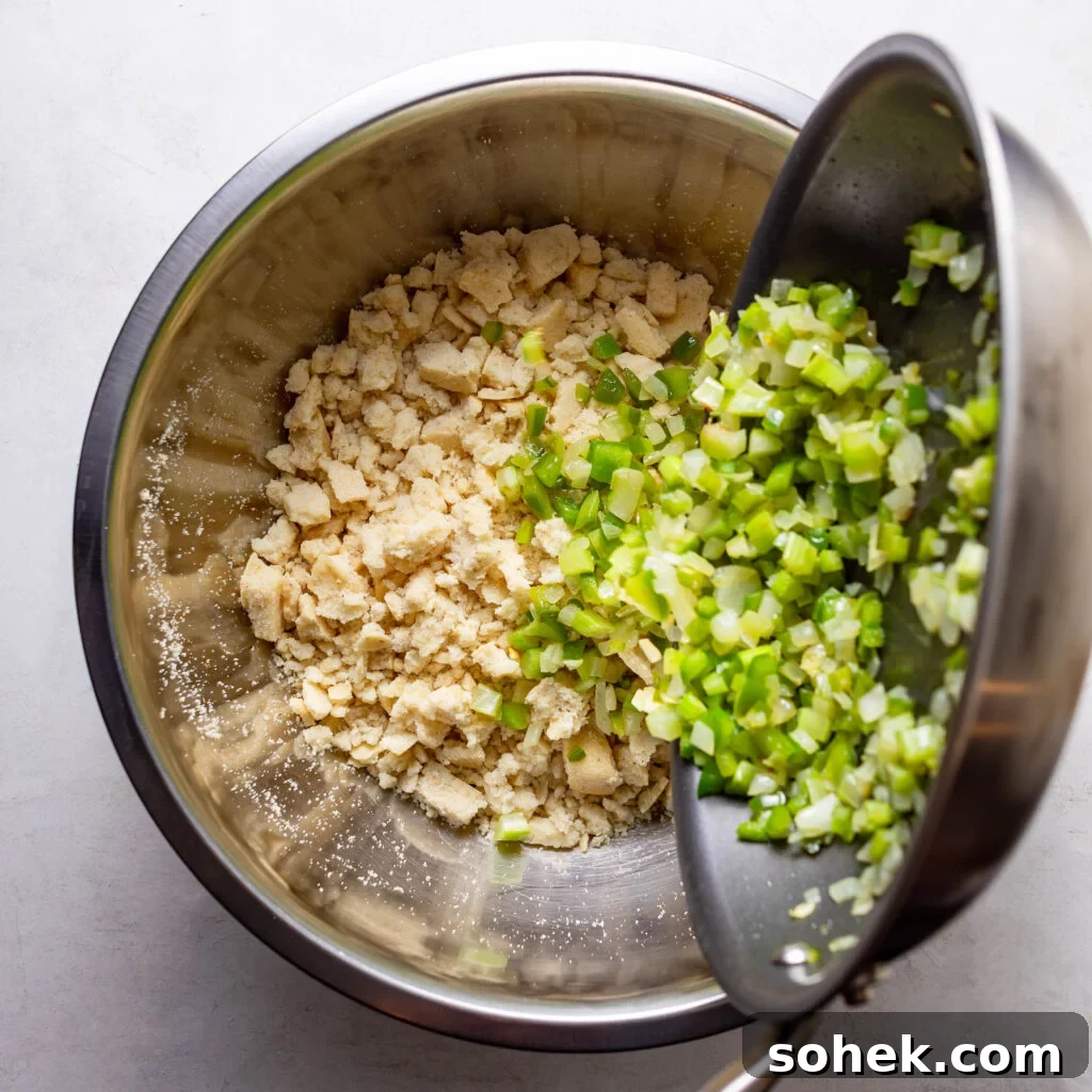 adding sautéed vegetables to cooked cornbread in a mixing bowl