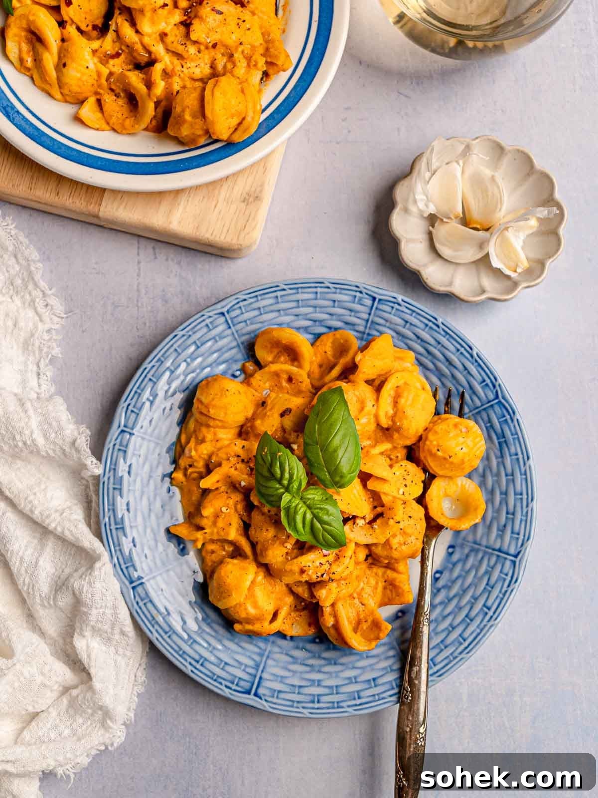 Creamy Pumpkin Pasta Sauce Recipe: Vegan, Savory Fall Dinner 9 Two servings of vegan pumpkin pasta with basil, styled with garlic cloves and a glass of wine.