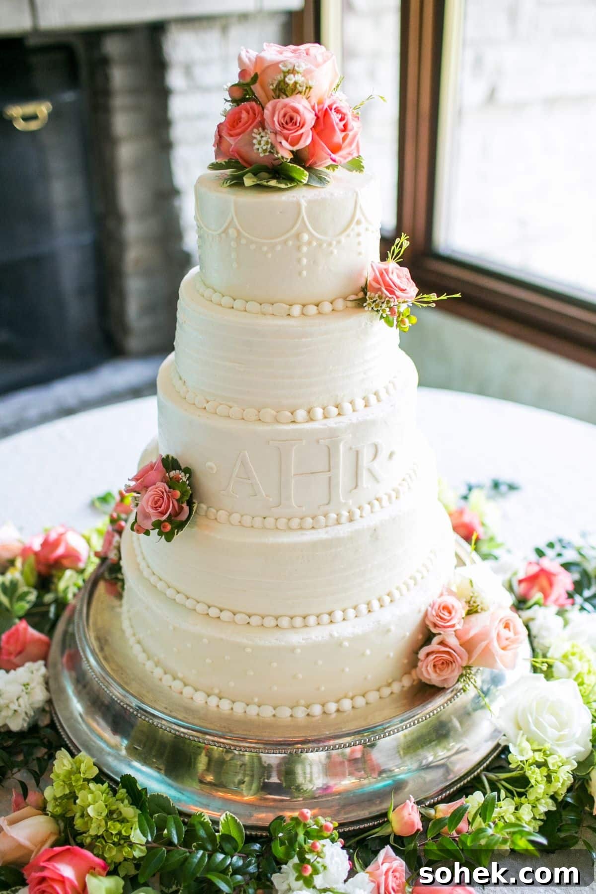 very feminine all white wedding cake with five layers, embossed initials, decorative piping, and miniature pink roses.