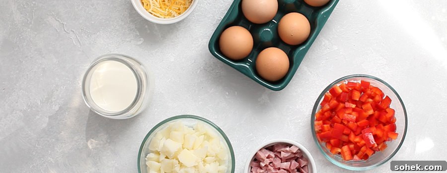 Top-down view of ingredients for egg muffins—eggs, shredded cheese, milk, diced potatoes, chopped ham, and diced red bell peppers neatly arranged in bowls on a light surface.