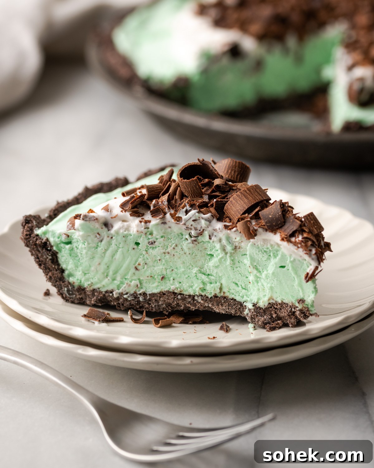 No-Bake Chocolate Mint Pie Recipe: Creamy No-Bake Mint Chocolate Pie 12 A slice of chocolate mint pie topped with whipped cream and chocolate shavings served on a white plate.