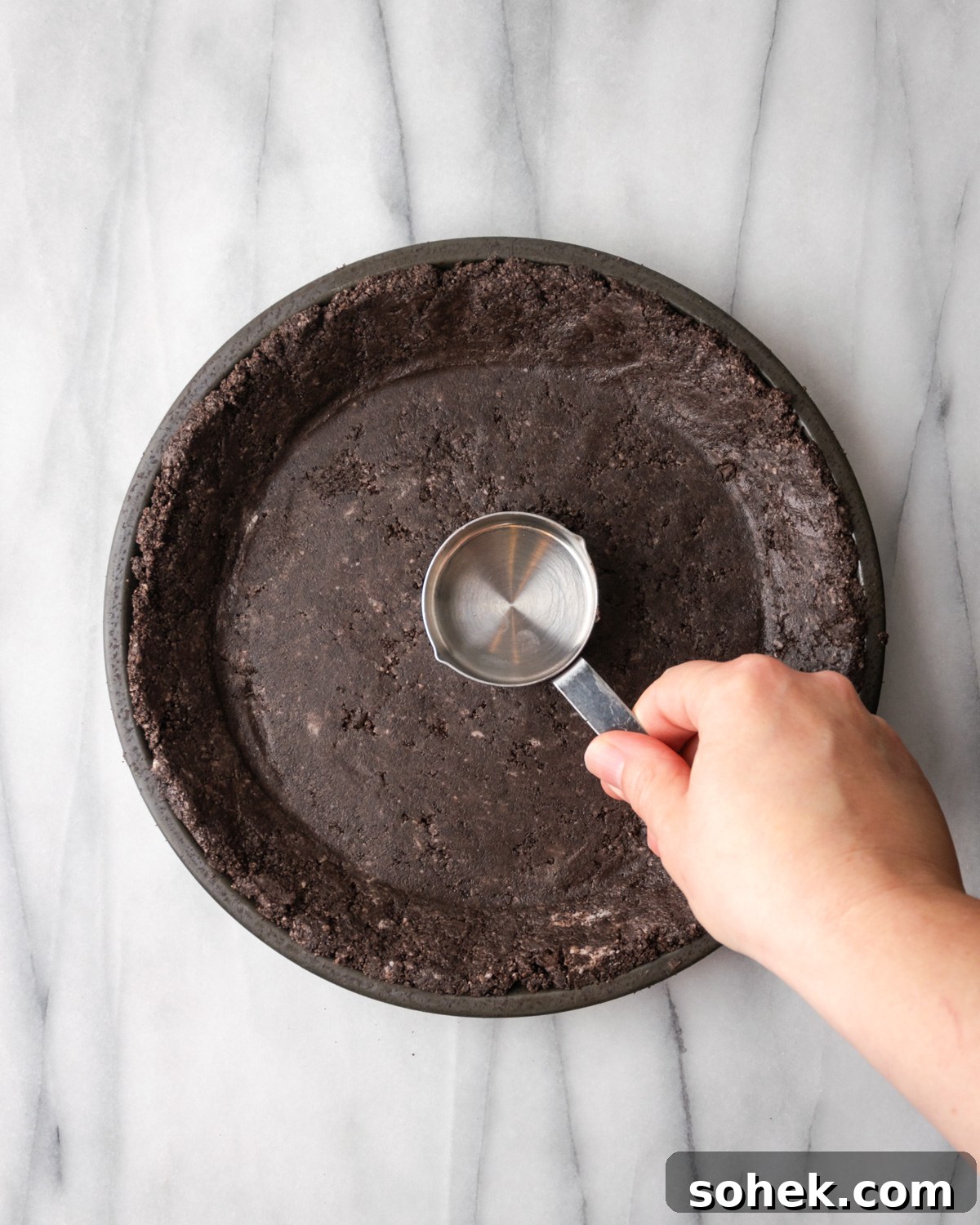 No-Bake Chocolate Mint Pie Recipe: Creamy No-Bake Mint Chocolate Pie 5 Orea and butter mixture being pressed into a pie pan with measuring cup.