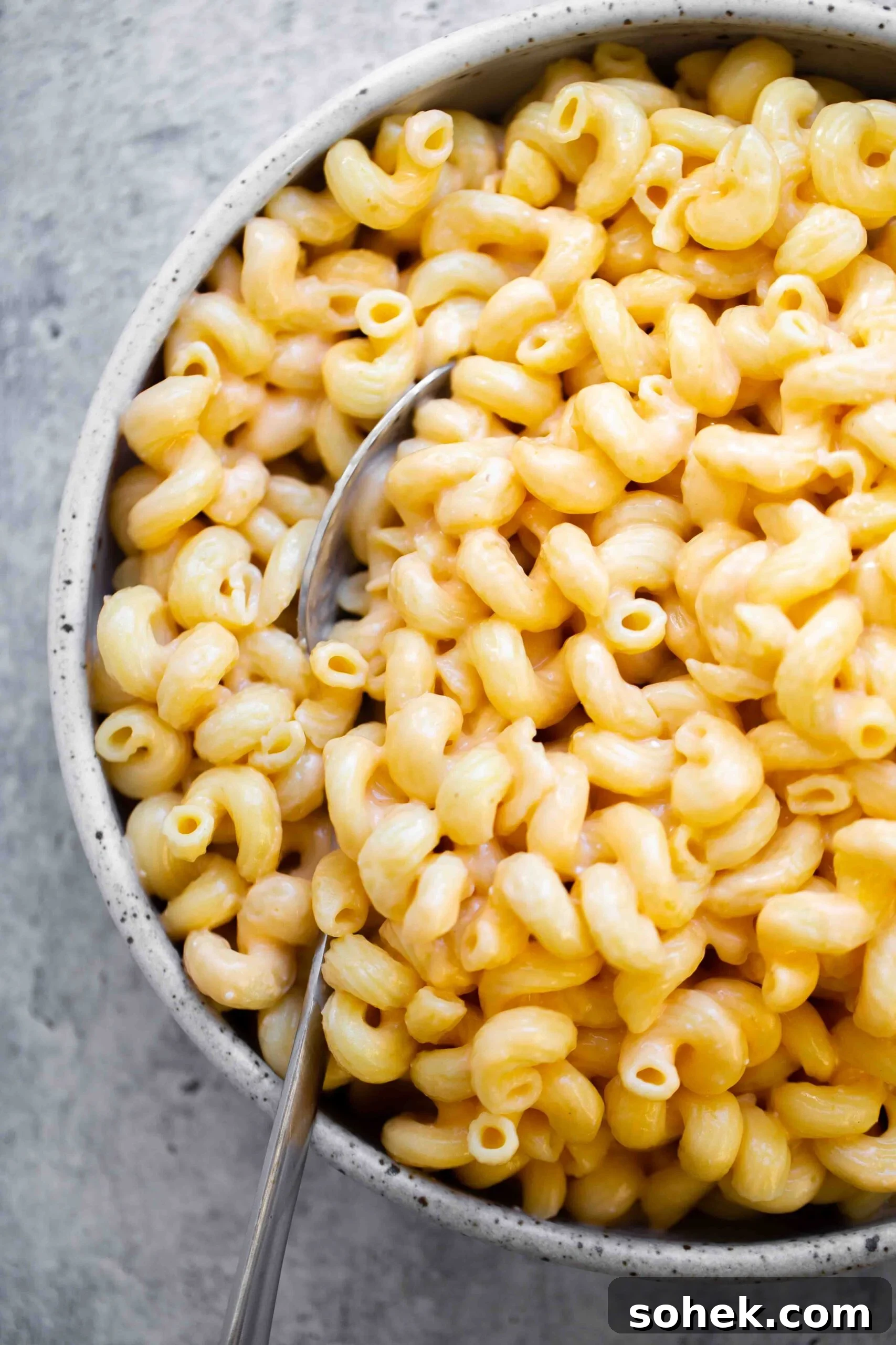 overhead photo of a creamy bowl of instant pot mac and cheese recipe with a spoon on a gray textured background