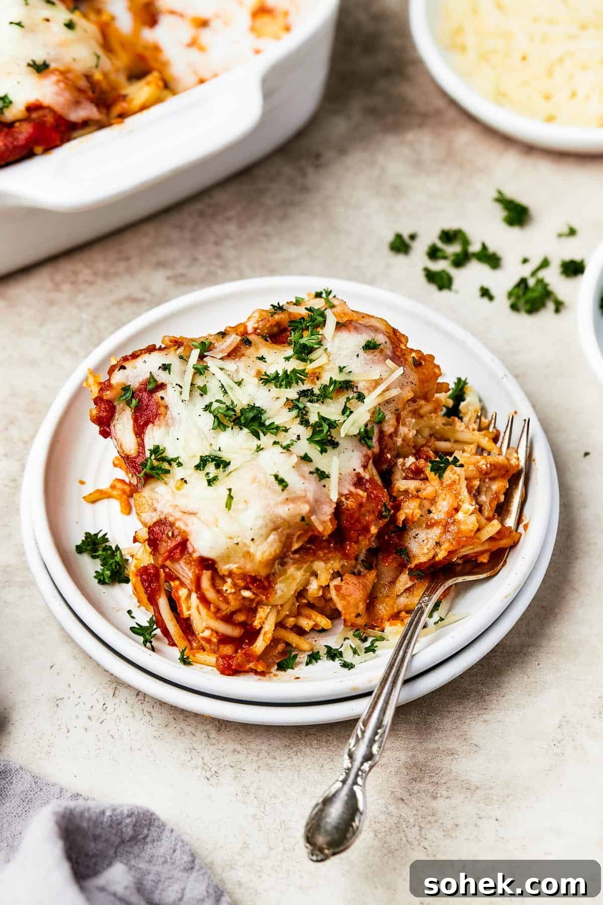 A square of baked spaghetti on a plate, garnished with parsley.