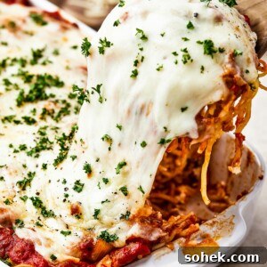 A portion of spaghetti bake being lifted from a casserole dish, with the cheese topping stretching.