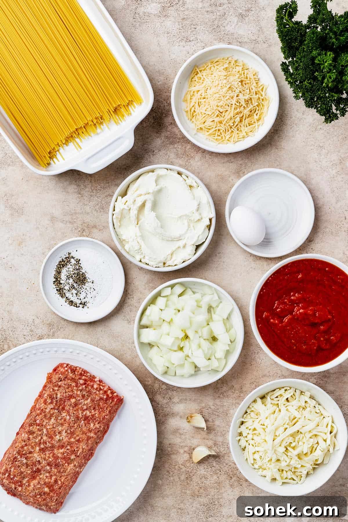 From top left: dry spaghetti, onion, seasonings, ricotta, an egg, mozzarella, marinara sauce, italian sausage, garlic, parmesan.
