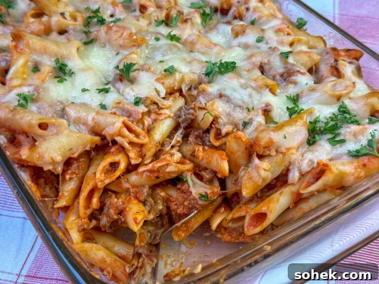 Penne pasta, Italian sausage, red pasta sauce, mozzarella cheese in an easy casserole on a red and white plaid napkin.