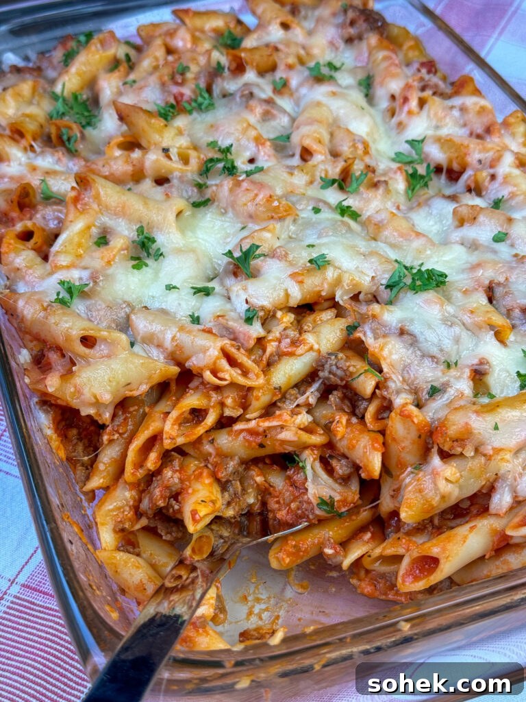 Serving spoon dipped into an easy mostaccioli recipe with cheese and Italian sausage.