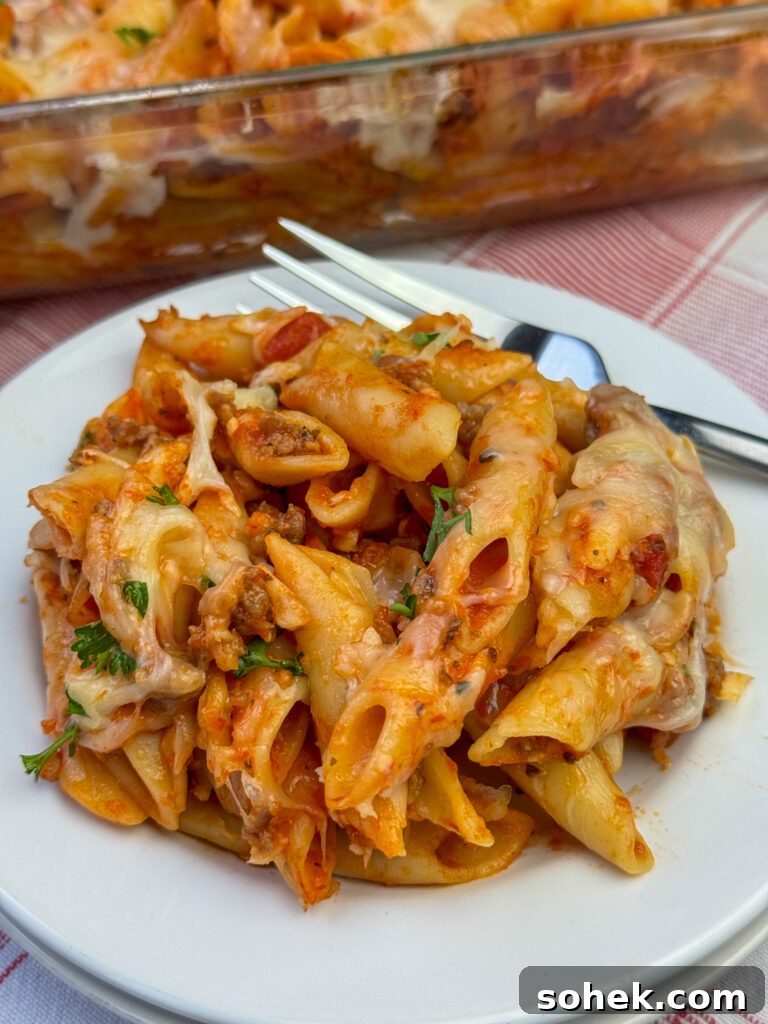 Overhead view of fork resting on a plate of cheesy pasta casserole with plenty of marinara sauce and ground beef on a stack of white plates.