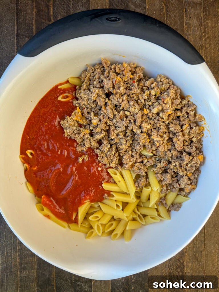 Cooked mostaccioli pasta with red sauce and cooked and crumbled Italian sausage poured into the large mixing bowl.
