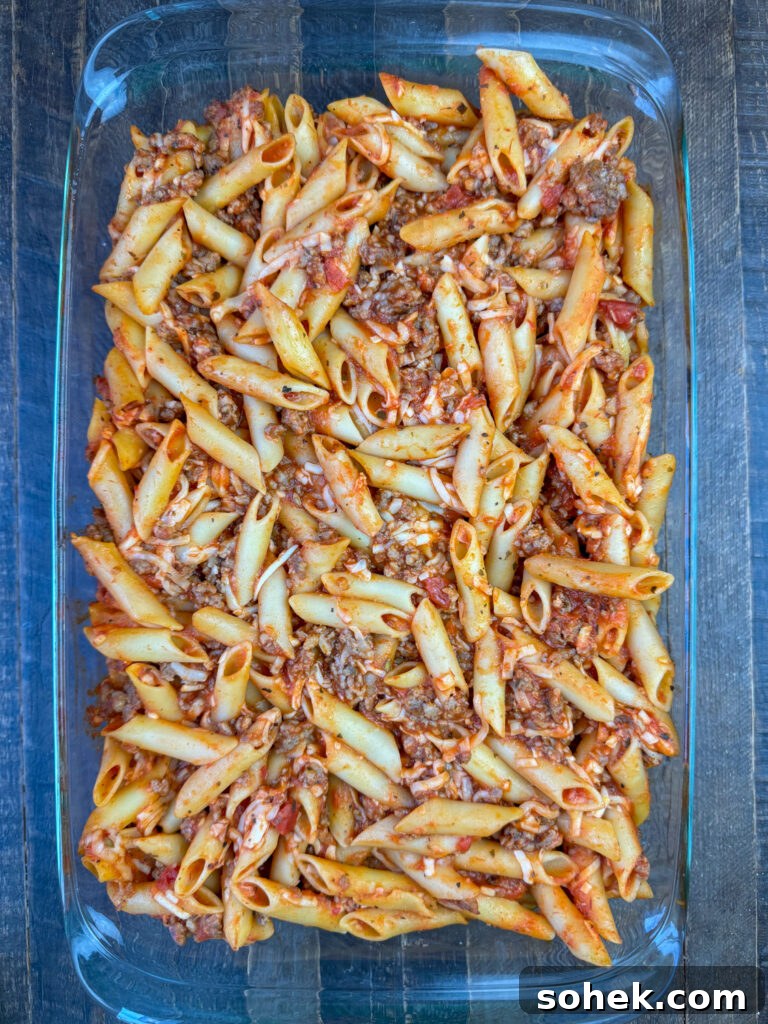 Smooth and tubular pasta in a 9 x 13 dish with easy ingredients to make a casserole on a wooden counter top.