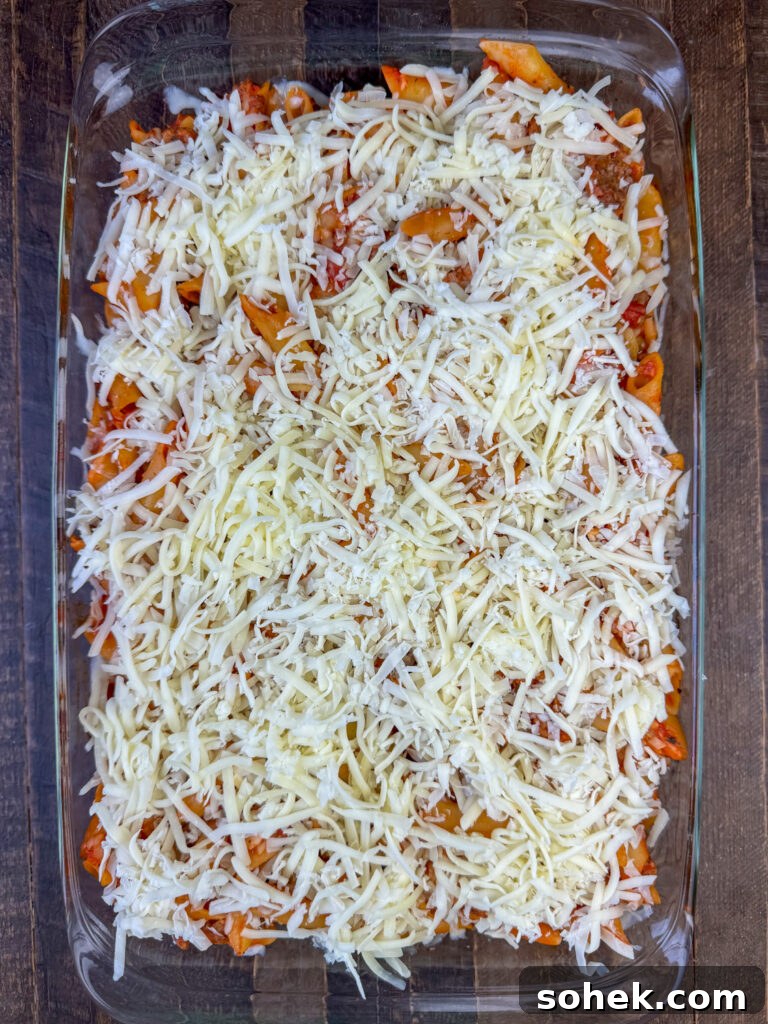 Thick layer of shredded mozzarella cheese sprinkled over top of mostaccioli ready to put in the oven.