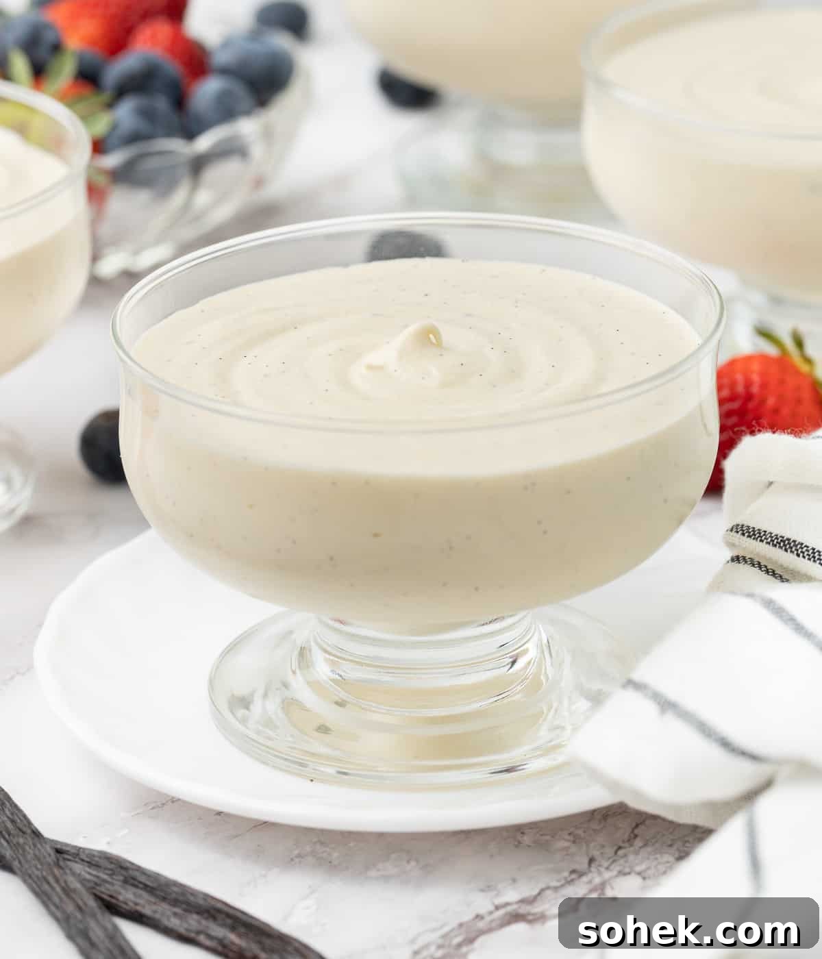 Mousse in a glass cup with three servings and a bowl of berries in the background.