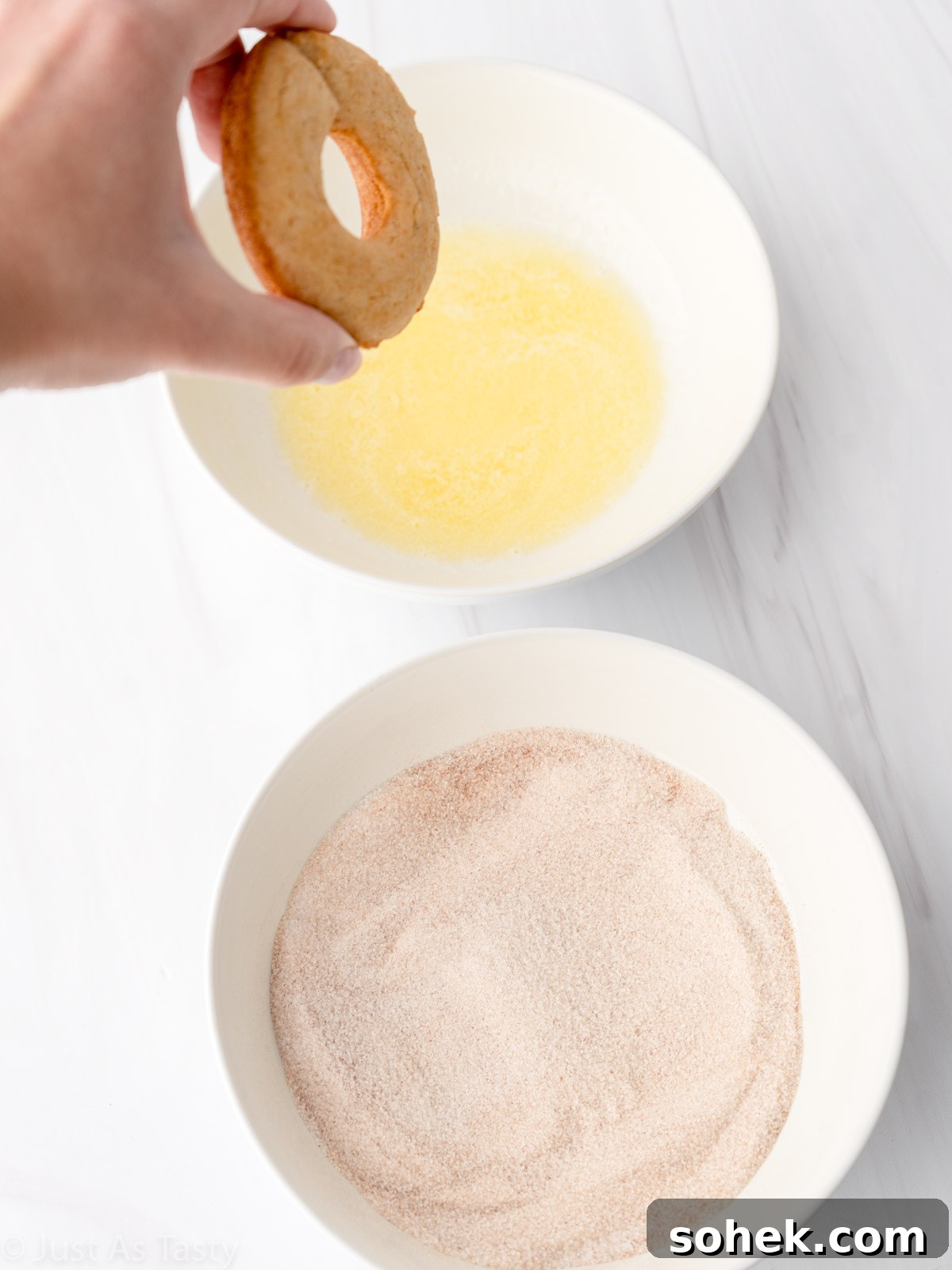 Donut being dipped into bowl of melted butter.