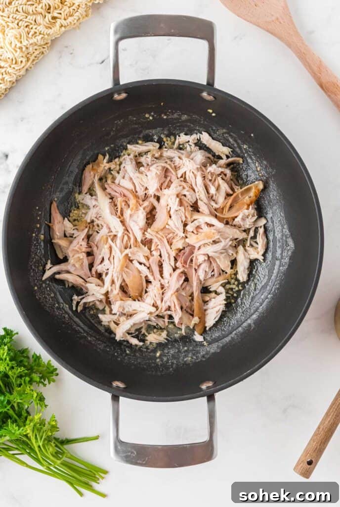 Shredded rotisserie chicken in skillet coated with garlic butter