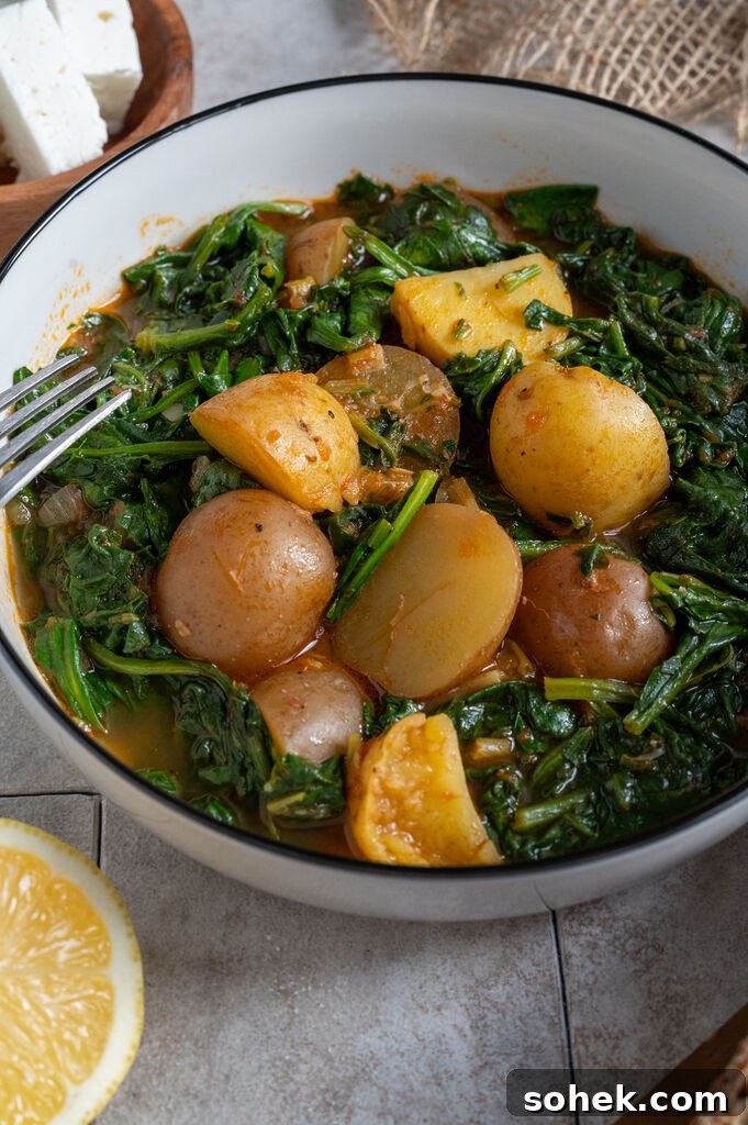 Spinach and potato stew in a white bowl, surrounded by feta, olives and bread.