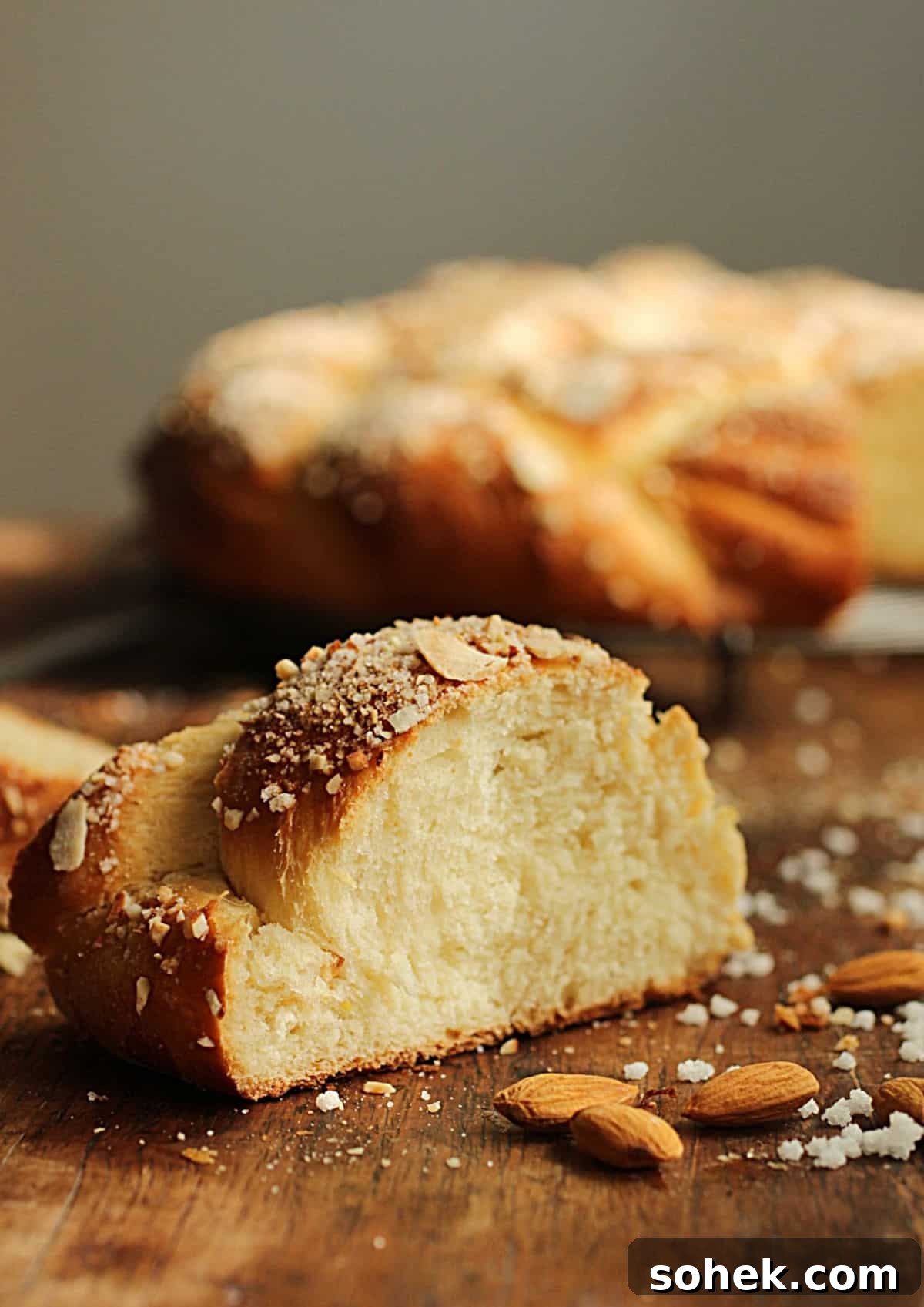 Slice of almond braid on a wooden table; whole bread in background.