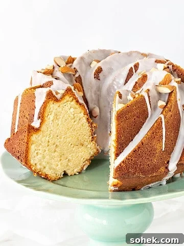 Almond bundt cake with glaze and slice missing on a green cake stand. White background.
