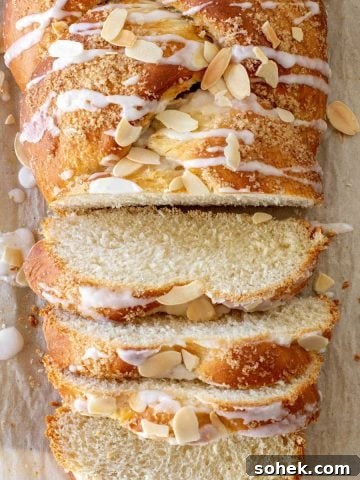 Beige parchment paper with sliced glazed almond Easter braided bread. Top partial view.