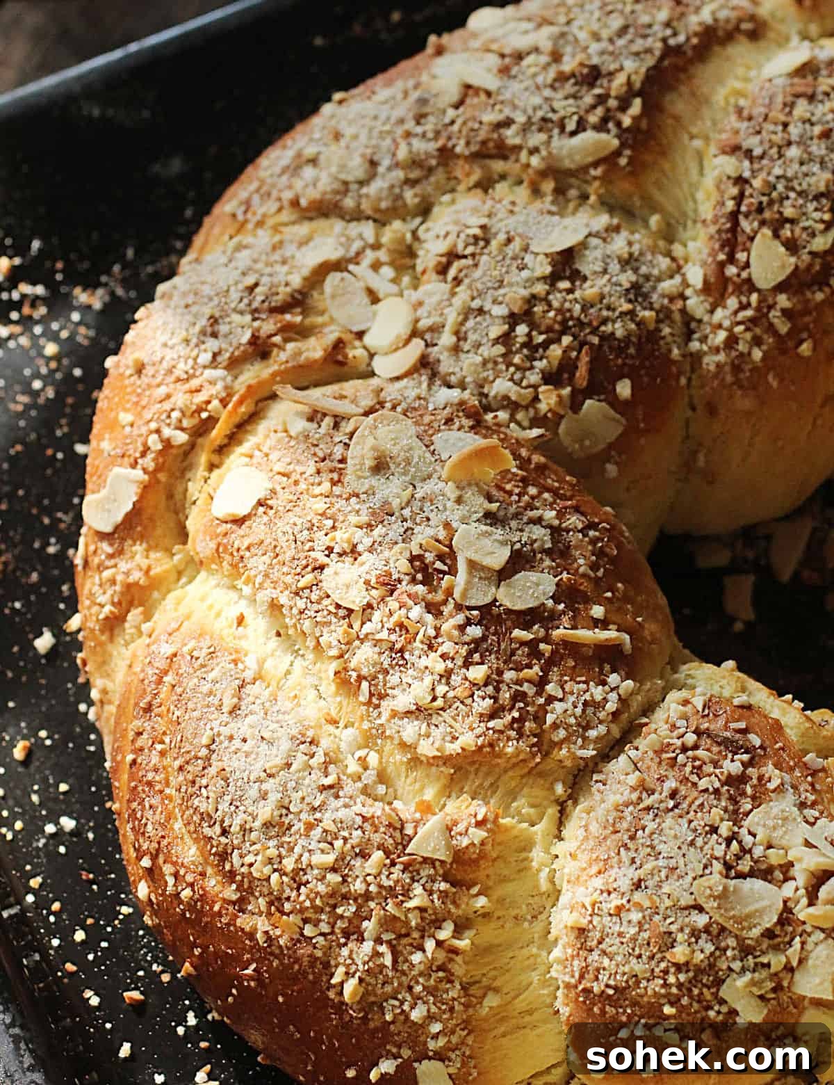 Top view of half baked almond braid on a black oven pan