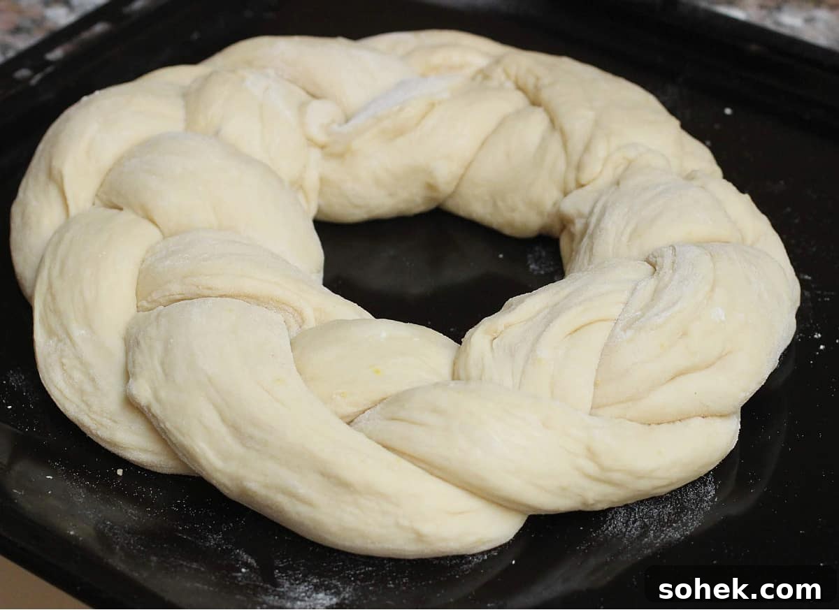 Braided round unbaked bread on a black oven sheet