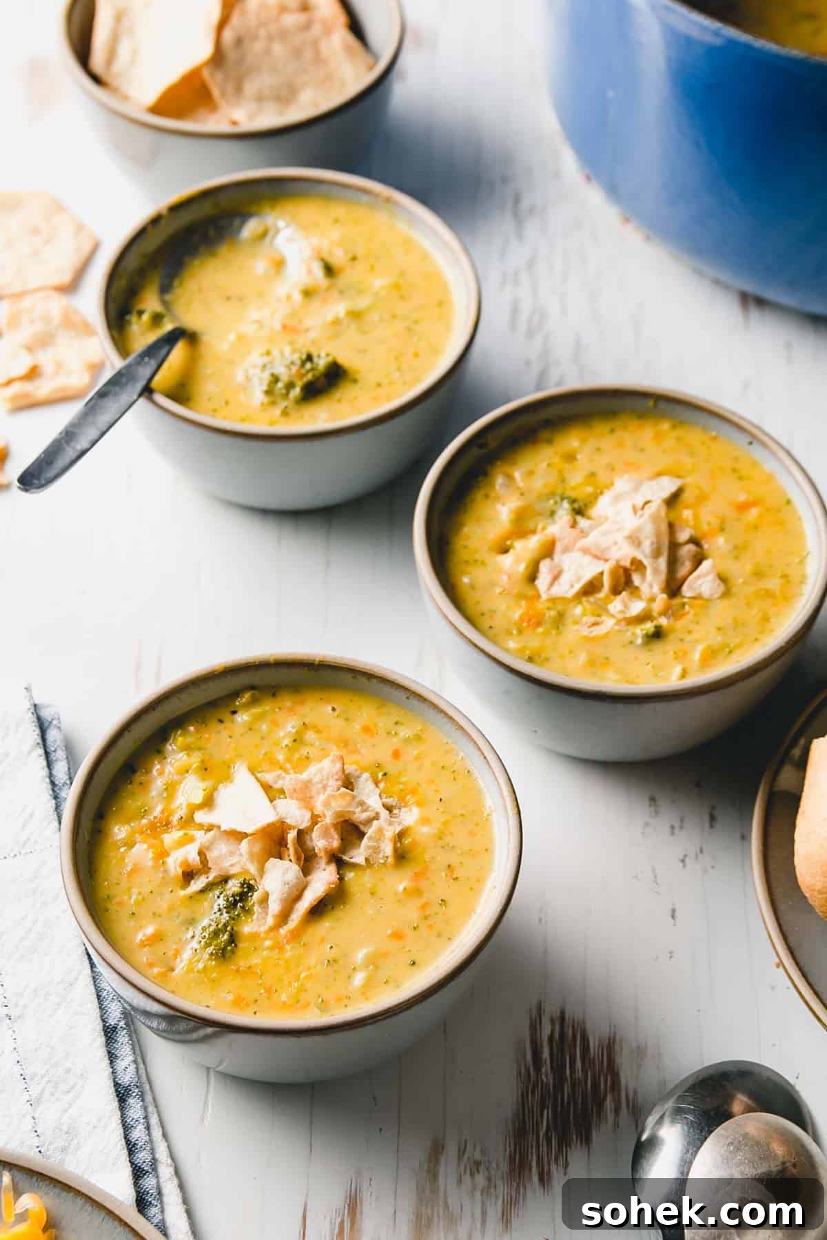 Three bowls of gluten free broccoli cheddar soup. Blue pot in background.