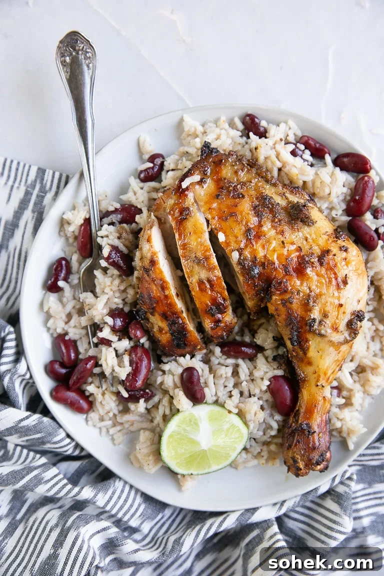 Overhead image of grilled jerk chicken on a white plate with Jamaican rice and peas.