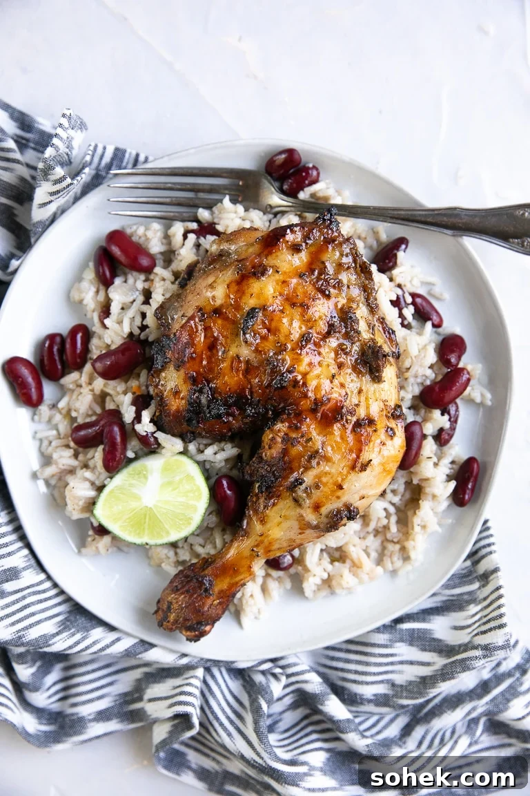 Overhead image of grilled jerk chicken on a white plate with Jamaican rice and peas.