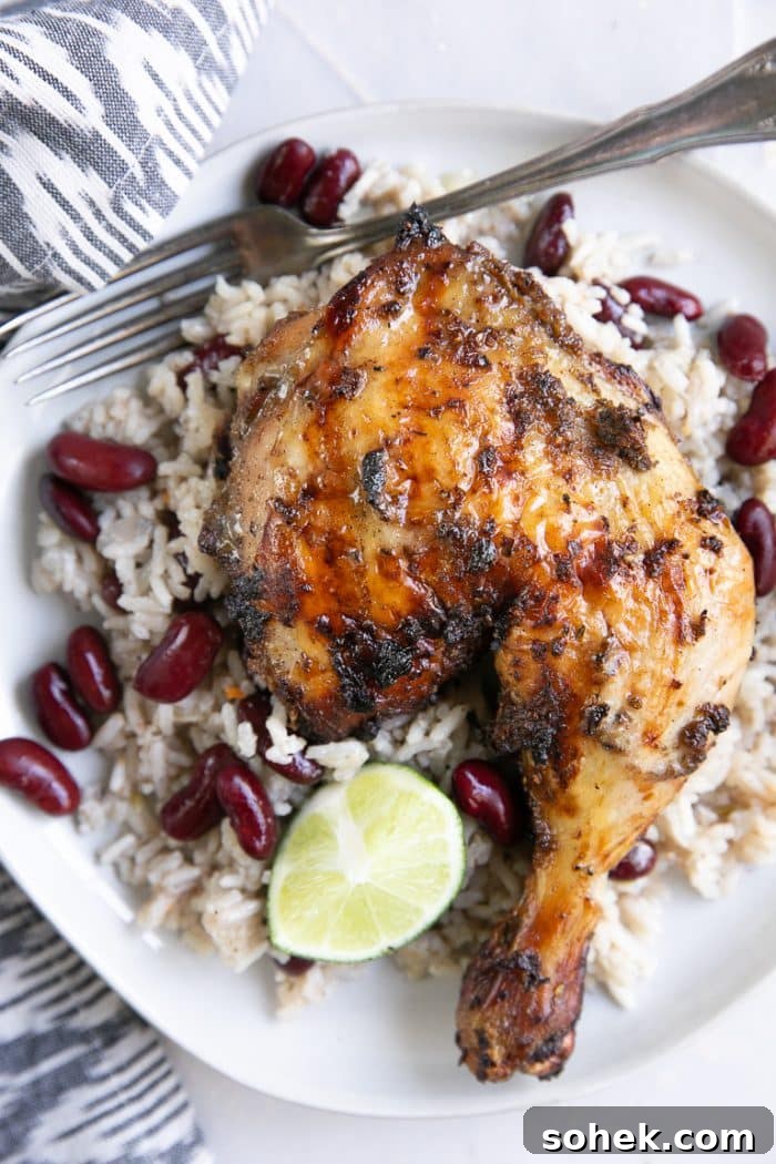 Overhead image of grilled jerk chicken on a white plate with Jamaican rice and peas.