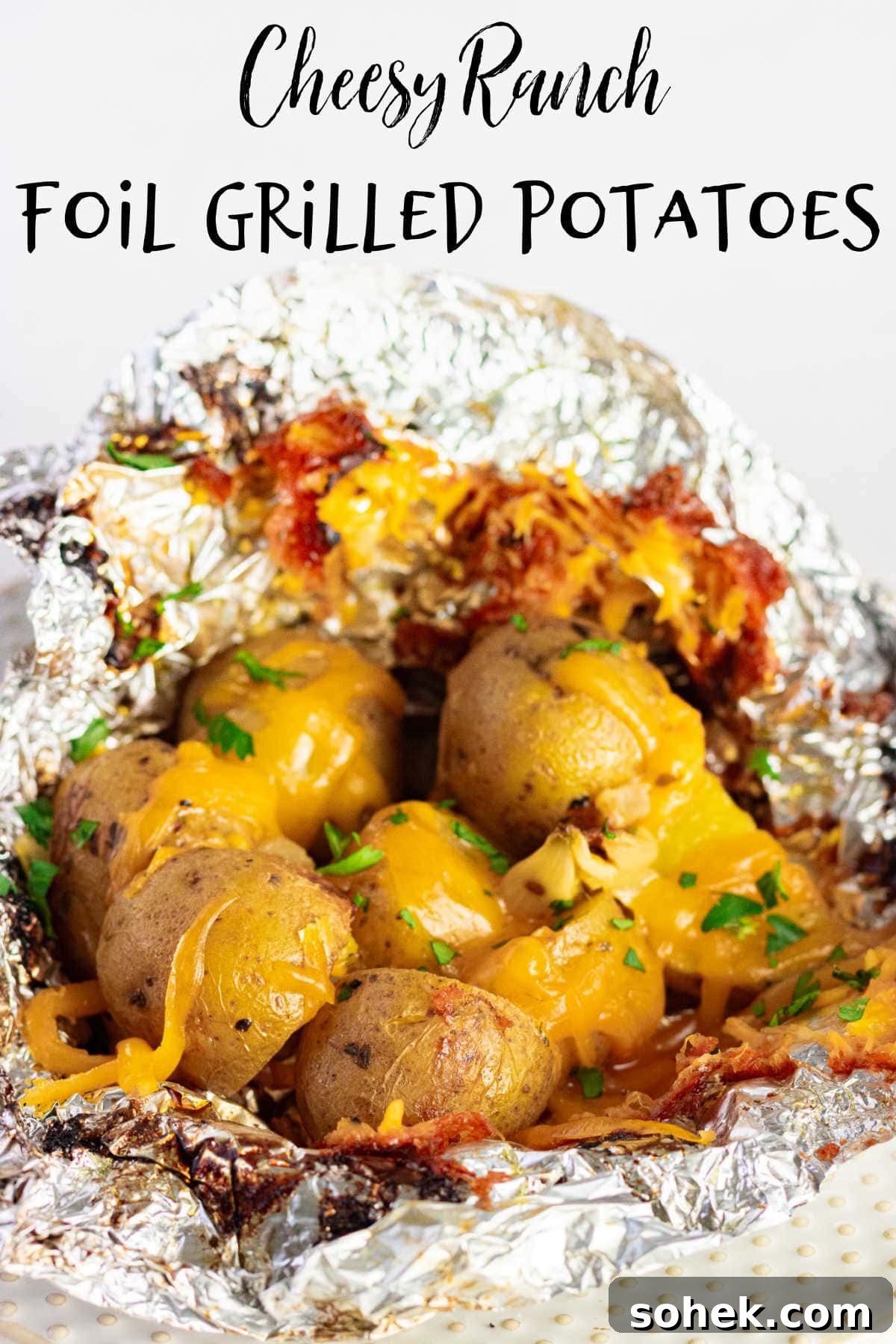 A closeup of cooked potatoes with cheese in an open foil packet.