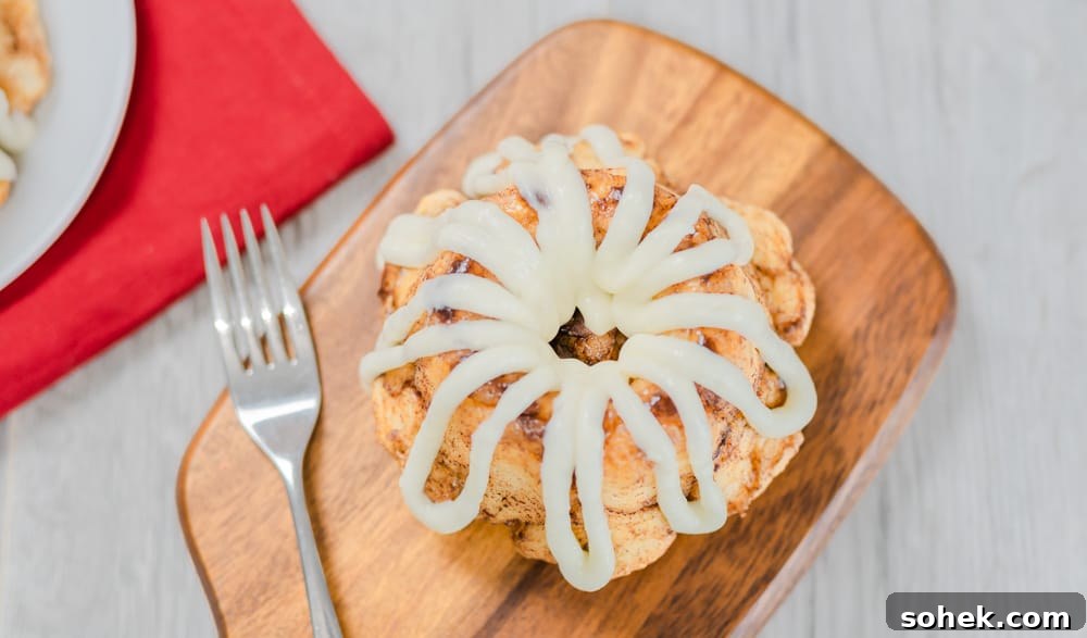 Mini bundt cinnamon sugar pull-apart bread with cream cheese glaze serving board fork with rose red napkin closeup.