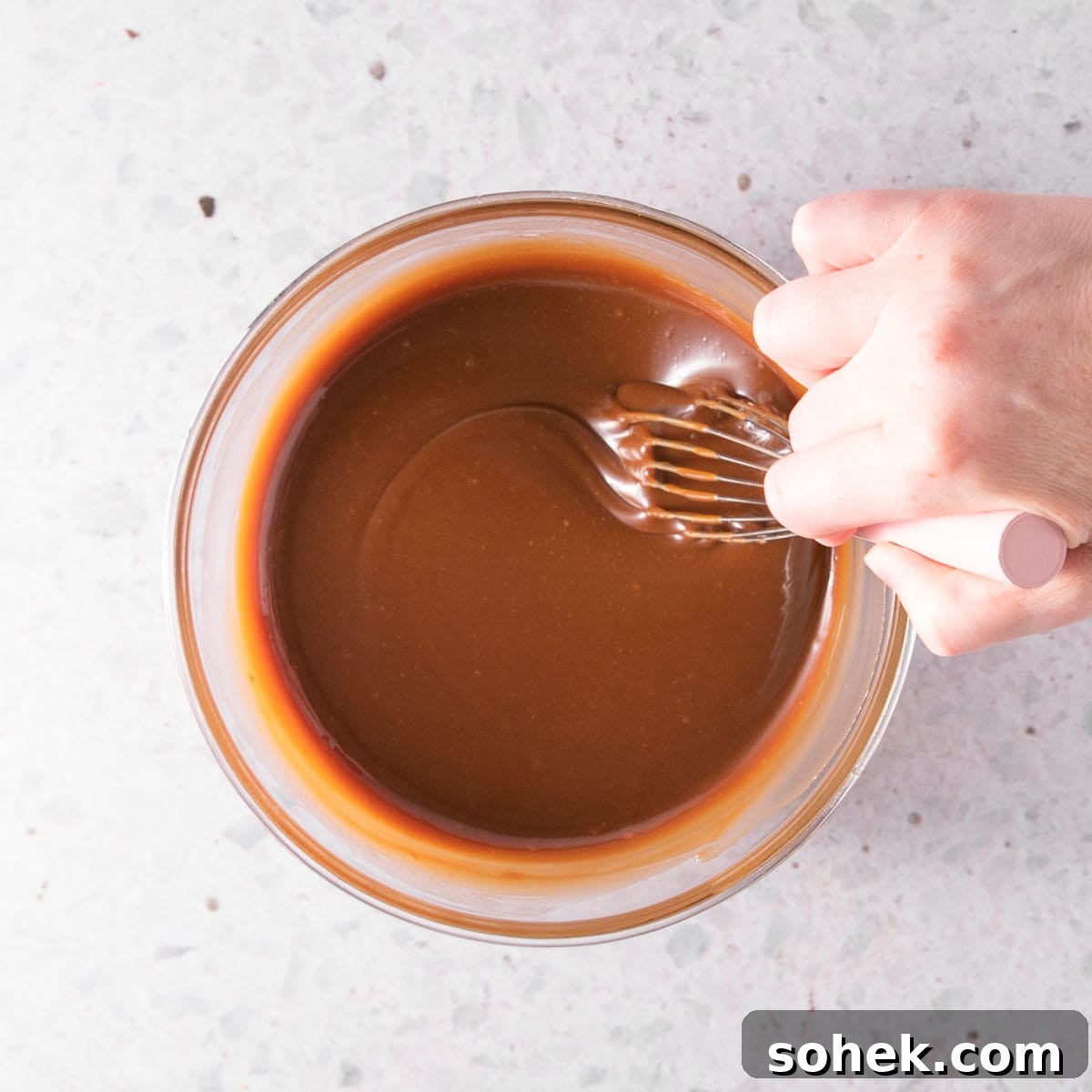 A hand stirring the finished sauce with a pink-handled whisk.