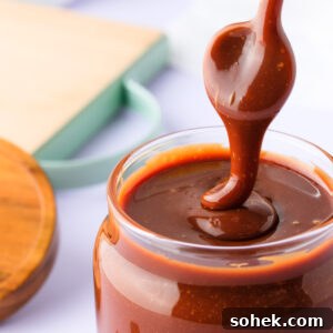 A close up of a jar of chocolate caramel sauce, with a spoon drizzling the thick sauce back into the jar.