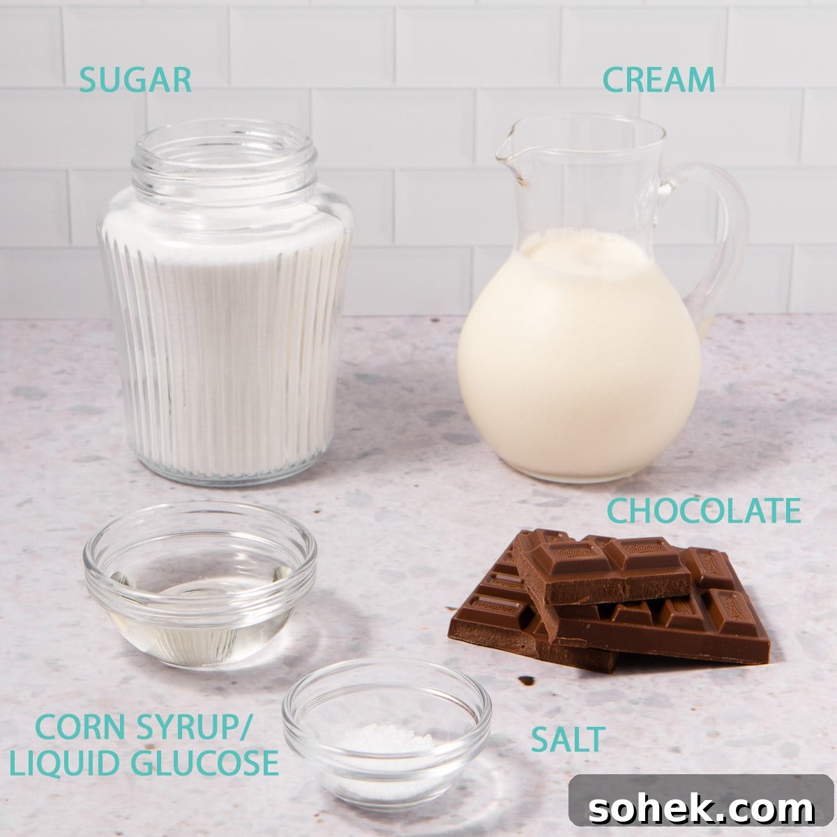 The ingredients for chocolate caramel sauce in glass containers on a grey background - sugar, cream, corn syrup, salt and chocolate.