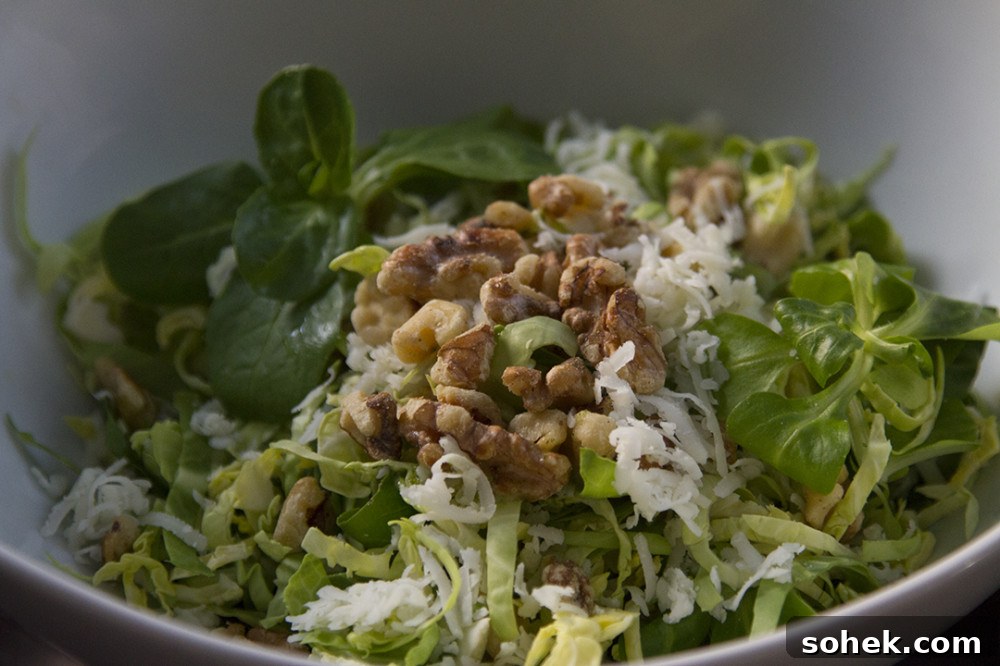Shaved brussels sprouts salad topped with walnuts and cheese in a white bowl.